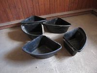 Four black plastic feed bins arranged on a concrete floor