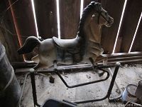Side view of vintage white and black metal rocking horse with visible rust and missing handle on base frame.