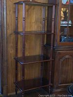 Front view of wooden four-tier open shelf with turned columns and polished finish.