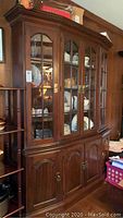 Front view of the wooden china cabinet showing three glass upper doors and three wooden lower doors, dark wood finish, brass handles.