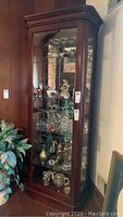 Front view of tall wooden curio cabinet with glass door and shelves, filled with decorative items (items not included).