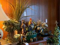 Wide view of all items on table including fox candle holder, brass frogs, wooden duck, rooster, flower frog, vase with faux flowers, and metal mugs.