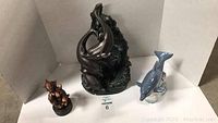 Overview photo showing all three dolphin items: large dark Austin dolphin sculpture with two smaller dolphin figurines (blue and brown)