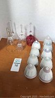 Photo showing 11 Lladro porcelain bells with white relief designs and four cut glass crystal and ruby bells on a wooden surface