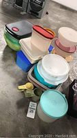 Full lot of assorted Tupperware pieces and related kitchenware stacked on concrete floor.