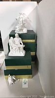 Multiple Lenox green and gold boxes stacked with Pietà and Guardian Angel sculptures displayed on top and lamb figurine in front