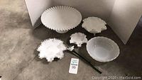 White milk glass items including cake stand, ruffled bowls, and glass hat item, arranged for display