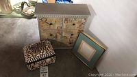 Photo showing all three items: wooden multi-drawer box, shell-decorated box, and framed shell picture leaning against wall