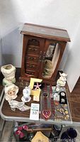 Overall lot including wooden jewelry box, assorted vintage ceramic lady figurines, and jewelry pieces on table
