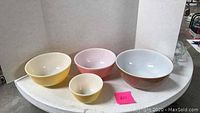 Four vintage Pyrex mixing bowls in yellow, pink, and brown with a patterned exterior brown bowl arranged in size order.