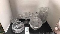 Six cut glass items including bowls, a decanter, a tumbler, and a lidded container on a black surface against white background showing detailed cut patterns