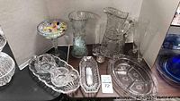 Full view of the lot showing various etched cut glass items and a compote bowl with colorful Murano glass candies and beads on a pedestal, placed on a table