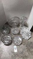 Cut glass collection arranged on floor showing six bowls and one tall vase with intricate cut patterns.