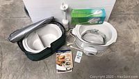 Full lot overview showing Crockpot, ceramic insert in green soft carrying case, mini blender in box, electric knife, instruction manual, and power cords on a concrete floor.
