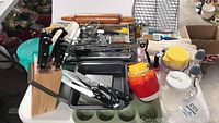 Wide view showing Berghoff knife block with knives, various baking utensils, plastic containers, rolling pin, and cooling rack on table.