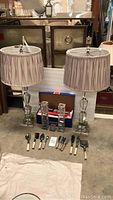 Full lot showing two glass lamps, box with glass candle holders, and serving utensils arranged in front