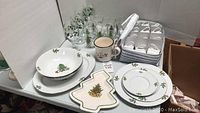Photo of Christmas-themed Pfaltzgraff dinnerware including plates, bowls, Christmas tree-shaped dish, glasses, and a mug arranged on table.