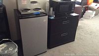 Side view of Daewoo mini refrigerator next to black cabinet with GE microwave on top