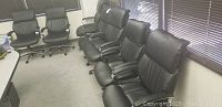 Seven black leather padded conference chairs arranged in a row in a room with blinds.