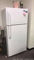 Front view of white Frigidaire top freezer refrigerator showing two doors with rounded handles, standing against a wall.