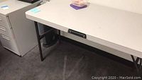 White Lifetime folding table with black metal legs seen from side angle near white file cabinet.