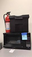 Photo showing stacked Westinghouse microwave, small portable file cabinet on top, and Kidde fire extinguisher beside them.