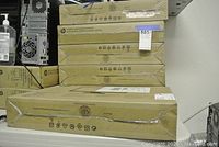 Stack of seven HP monitor boxes and one on shelf below, all sealed