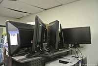 Side view of multiple assorted computer monitors lined up on a pegboard shelf showing their backs and bases