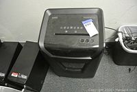Front view of black Staples shredder with control buttons visible on top and note with lot number attached.