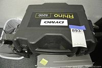 Closed hard plastic carrying case labeled Rhino 5200 by Dymo with auction tag on top.