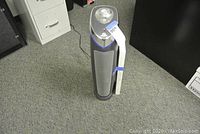 Front view of GermGuardian AC5000 air purifier with replacement filter element attached to side, on carpeted floor with electrical cord extended.