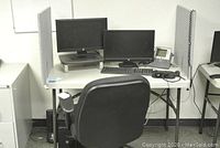 Front view of folding table with two HP monitors on top, desk phone, and adjustable black office chair.