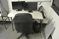 View of the white folding table with two HP monitors on it, a black office chair in front, and a phone on the table's right side. CPU tower under table.
