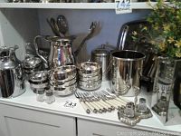 Photo showing metal bowls, dessert bowls, white plastic handled cutlery, forks, spoons, beverage dispenser, salt and pepper shakers, and gravy boats arranged on a white surface.