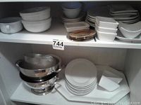 Various white bowls, side plates and dinner plates arranged on a shelf.