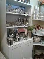 White melamine storage cabinet with multiple silver and metal items on open shelves, shown from front