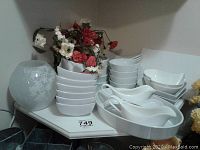 Image showing multiple white dishware pieces arranged on a shelf, including stacks of bowls, rectangular plates, gravy boats, and serving platters, with meausrement scale visible.