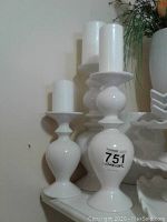 Three white ceramic candle holders of different sizes displayed with white pillar candles, showing shape and scale.