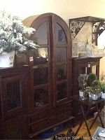 Front view of closed cabinet showing arched top, glass-pane doors and two lower drawers with surrounding decor