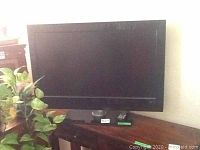 Front view of Philips television, black flat screen on glass stand, remote control in front.