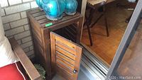 Wooden patio cabinet with slatted door, door open showing storage inside, signs of wear