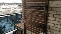 Two tier wooden outdoor patio shelving mounted on wooden slatted wall panel on balcony. Showing wood slats and shelves secured into brick wall.