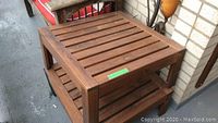 Two wooden patio side tables positioned on a concrete patio floor against a white brick wall. Tables have a slatted design with visible wear and scratches on wood surfaces.