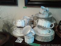 Porcelain china set displayed stacked and grouped, showing cups, saucers, plates, and bowls with gold trim on white porcelain.