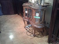 Side angled view of the oval wooden cabinet with visible intricate carved trim and glass front and side doors; showing power cords on floor nearby