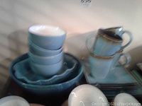 Stack of bowls, plates and cups in teal with brown rim, showing bowls and serving bowls.