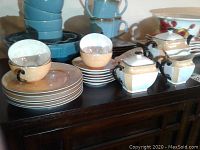 Photo of entire set showing cups stacked inside saucers, bread and butter plates stacked beside them, creamer, sugar bowl, and teapot arranged on a table