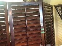 Front view of three panel espresso stained wooden louvered screen with horizontal slats and hinged panels.