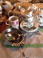 Set of Redoute Roses teacups, saucers, mug, and teapot arranged with metal serving spoon and bowl