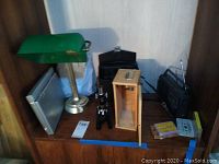 Wide view of lot items placed on wooden surface including microscope with wooden case, DVD player, binoculars, table lamp, radio, cassette tape, and cables.